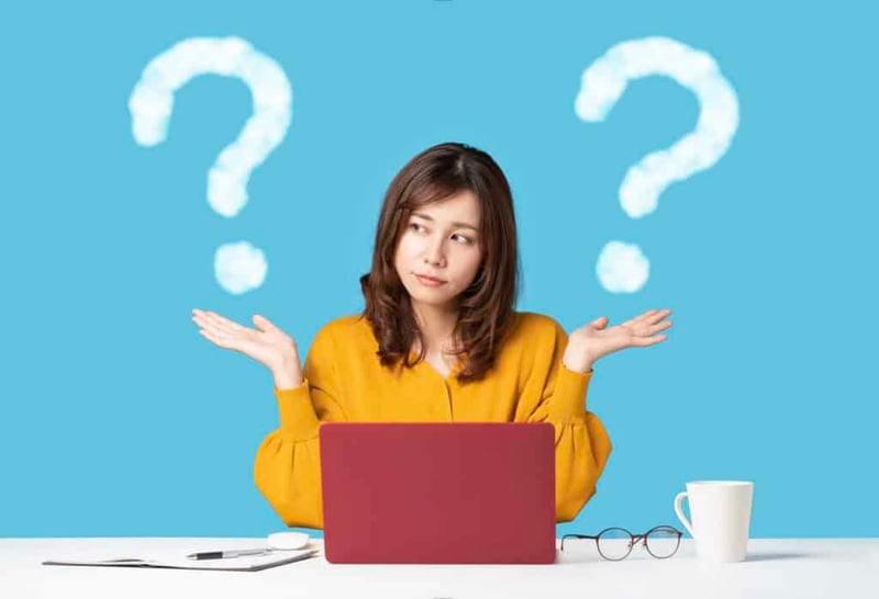a woman at a laptop shrugging, with question marks around her head