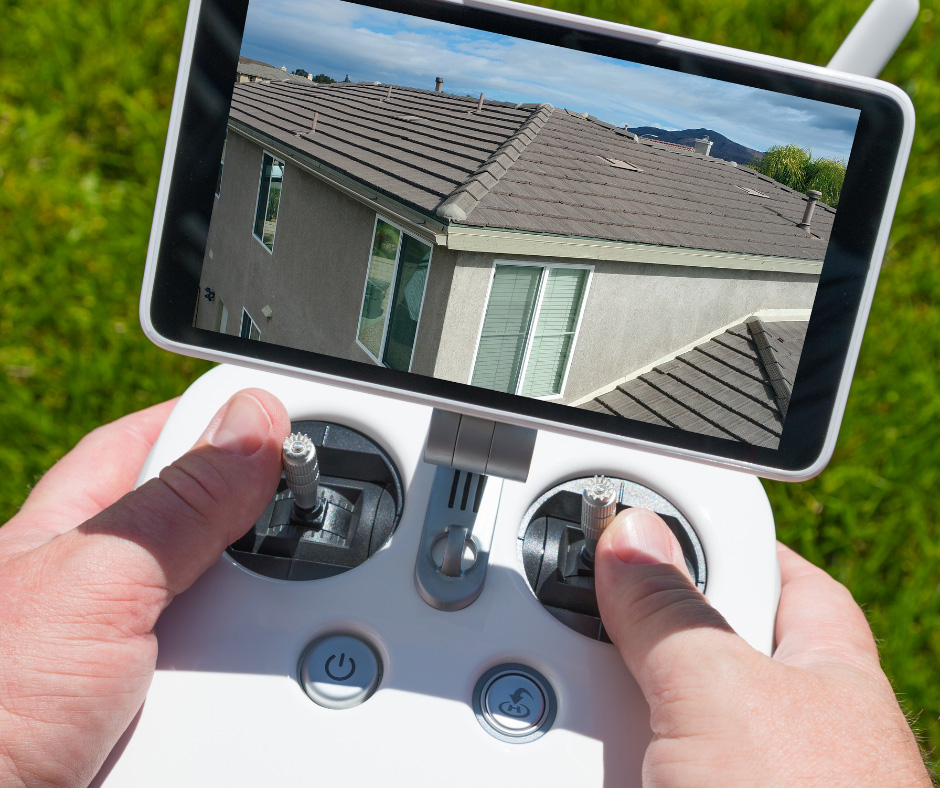 hands operating the controls of a drone; the screen shows a rooftop