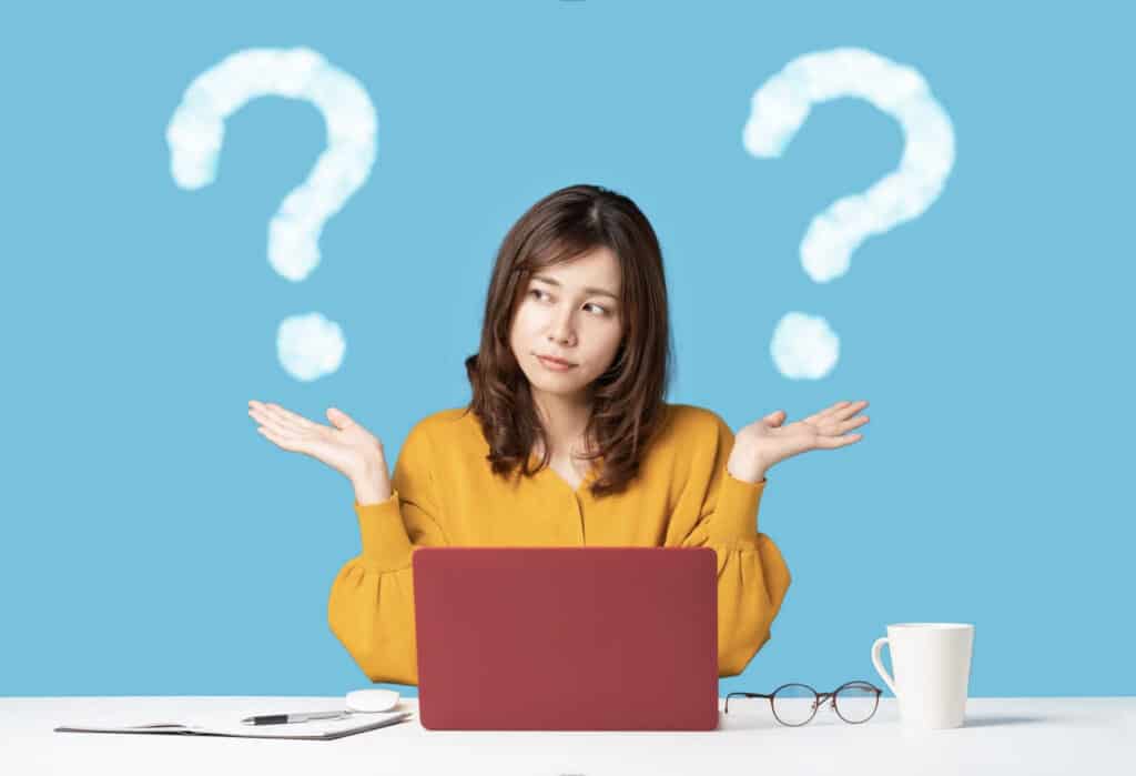 a woman at a laptop shrugging, with question marks around her head